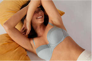 Model laying down and laughing in ThirdLove's Matte and Shine Balconette Bra in a silvery light blue color.